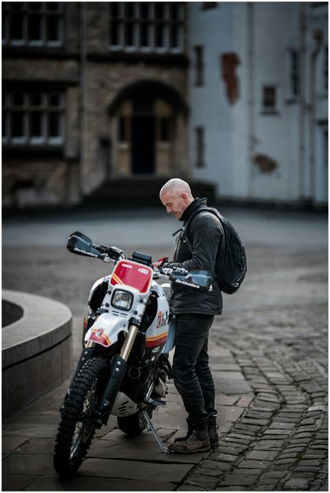 A man with a motorcycle outdoors in an urban plaza