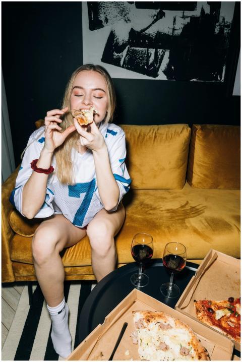 A young woman enjoys pizza and wine on a comfy cou