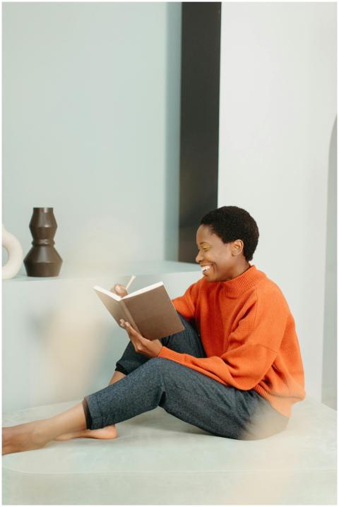 Woman sitting indoors, smiling, and writing in a n