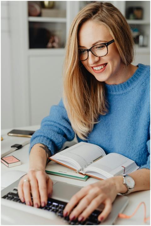 Smiling woman in eyeglasses typing on laptop at de
