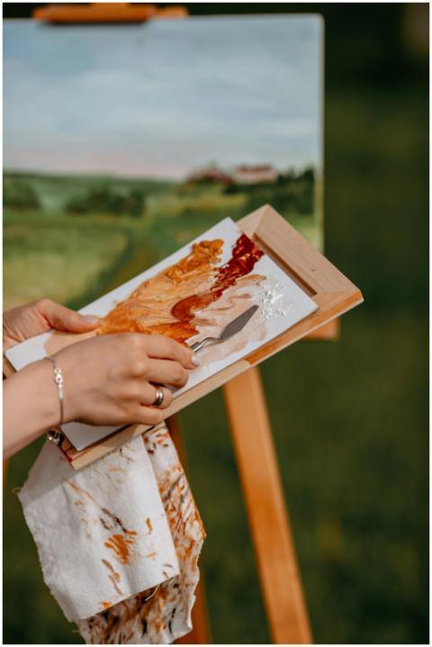 Artist holds palette while painting landscape outd