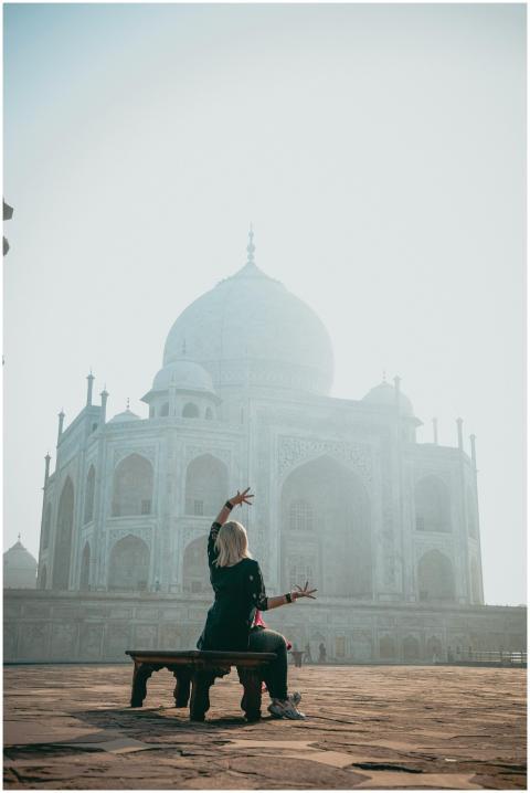 A woman poses with raised arms in front of the Taj