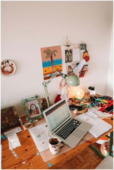 A well-used desk setup with a laptop, lamp, and pe
