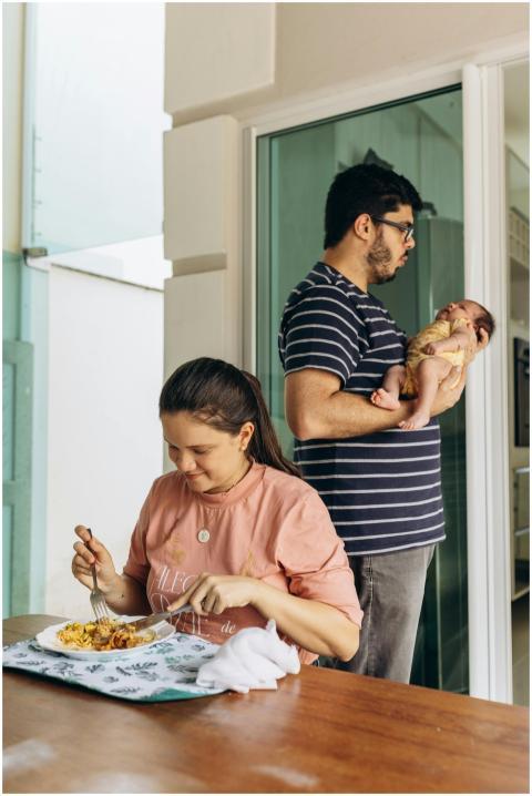 Father holding newborn while mother enjoys a meal,