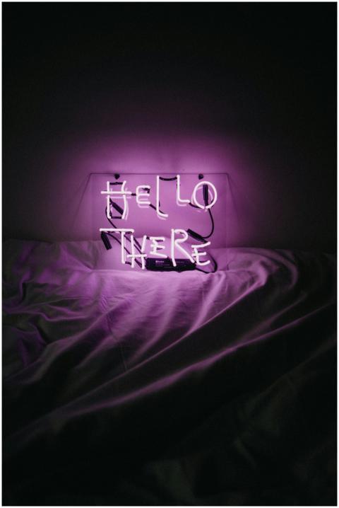 Purple neon 'Hello There' sign glowing on a bed, c