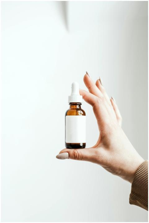 A hand holding a minimalist dropper bottle on a wh