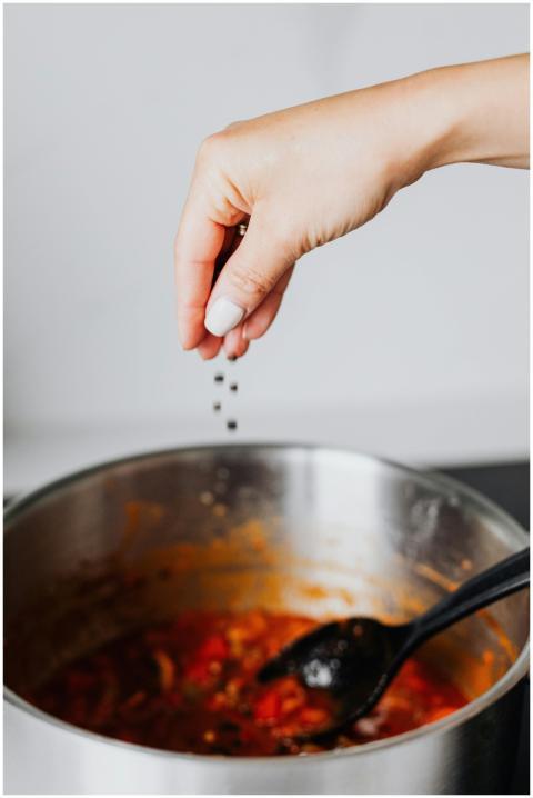 A hand seasoning tomato soup with black pepper in