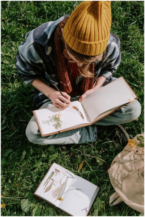 Person sitting on grass, writing in journal outdoo