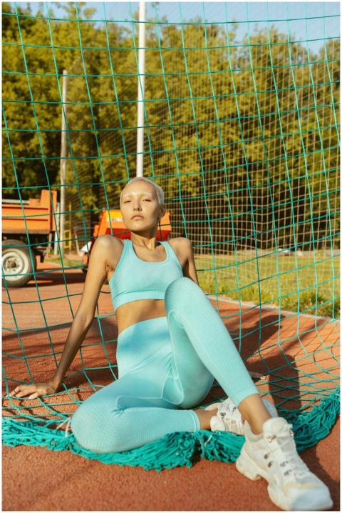Sporty woman in activewear resting against a net i