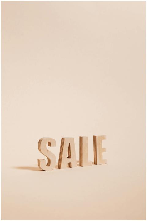 Wooden letters spelling SALE on a neutral beige ba