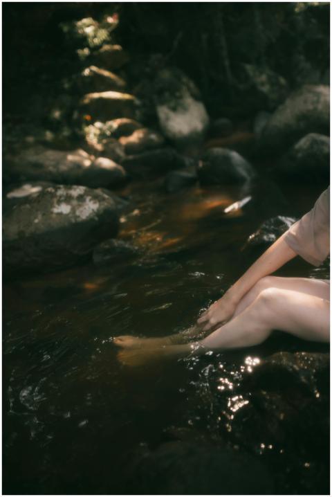A woman sitting by a tranquil stream, dipping her