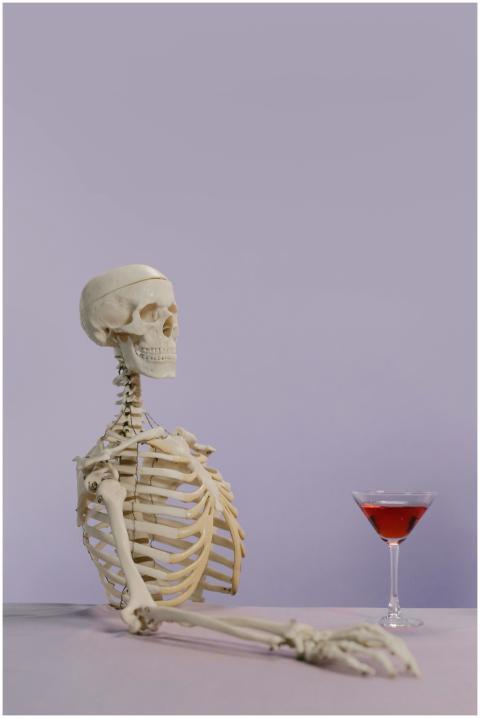 Skeleton model with a cocktail glass on a purple b