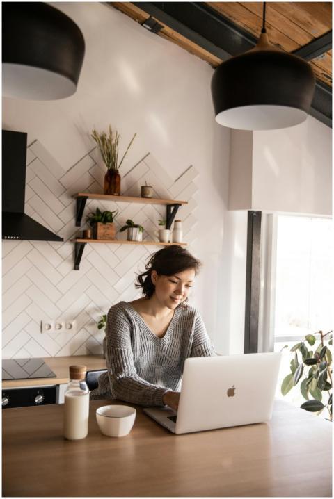 Young woman in cozy kitchen using laptop. Bright,