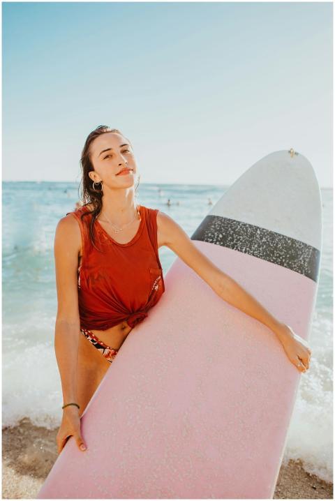 Confident woman holding a pink surfboard at a sunn