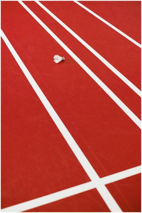 A lone shuttlecock lying on a red running track wi