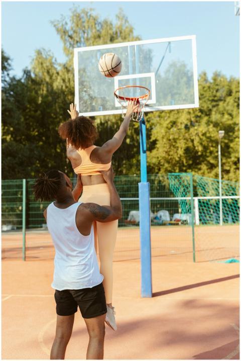 A man lifts a woman as she shoots a basketball on