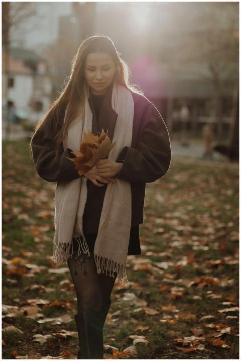 Young woman holding autumn leaves in a park, sunli