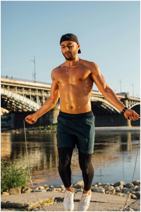 Muscular man skipping rope by river under clear sk