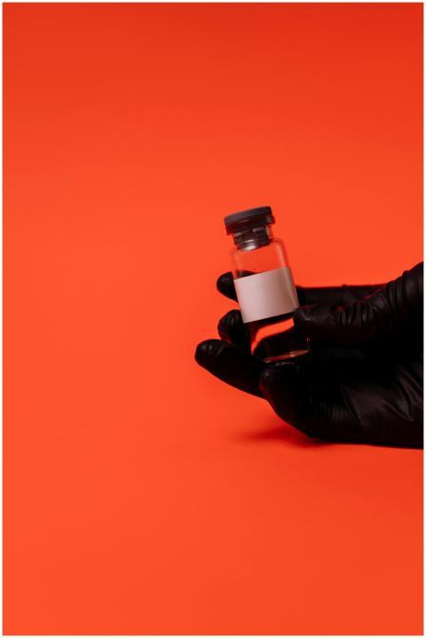 A gloved hand holding a vaccine vial against a vib