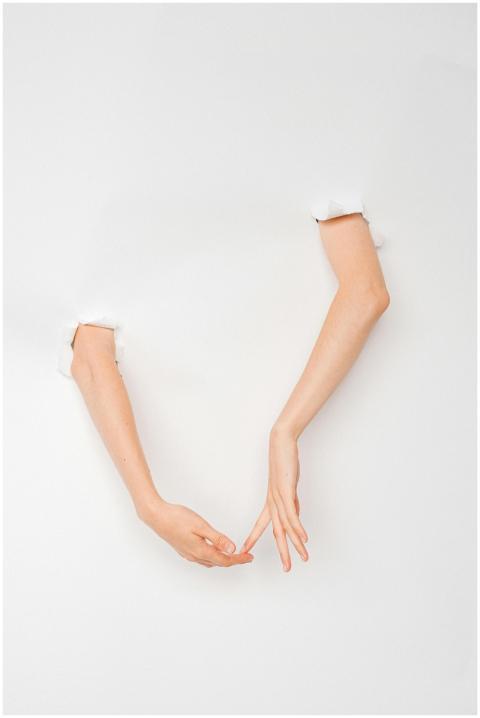 Two hands reach through torn paper, creating a con