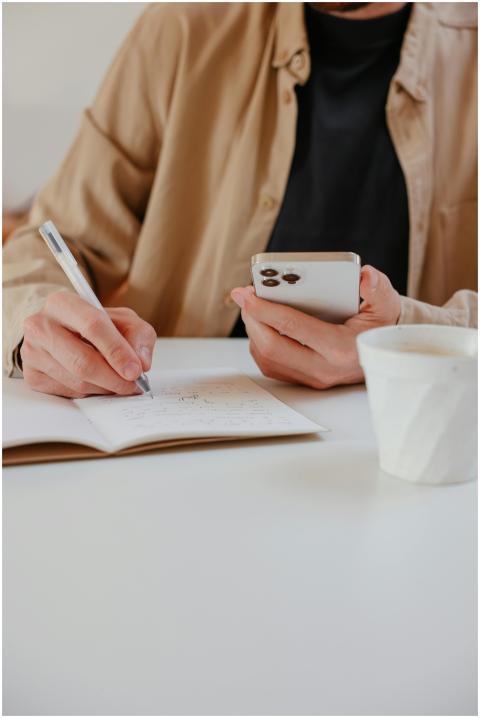 Man taking notes on a notebook while using a smart