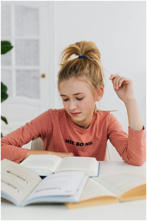 A young girl engrossed in reading books indoors, d