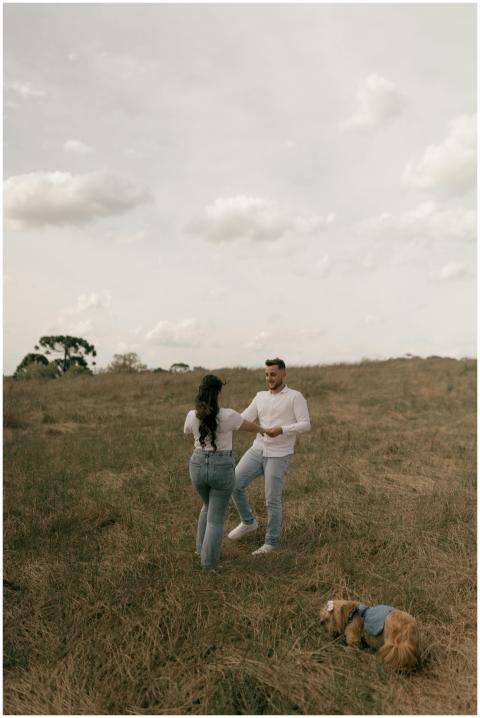 Man and woman dancing in a field with playful dog