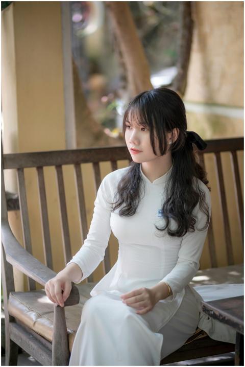 A young woman in a white traditional dress sits gr