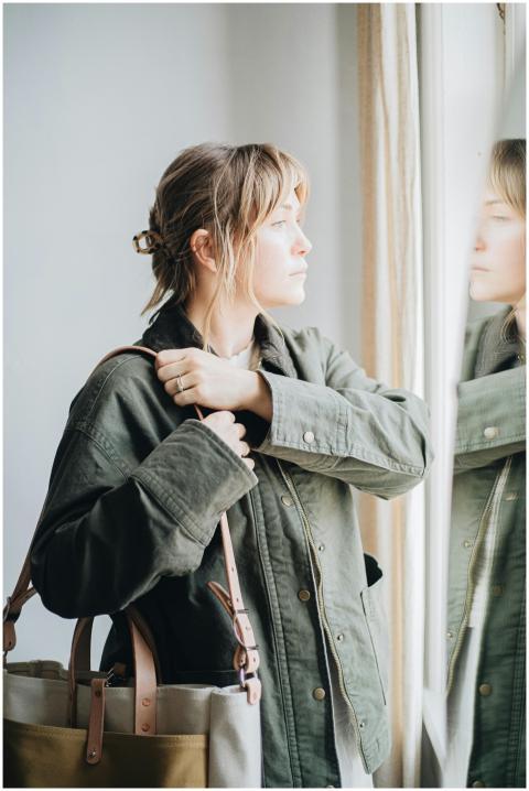 A woman in a green jacket gazes out a window besid