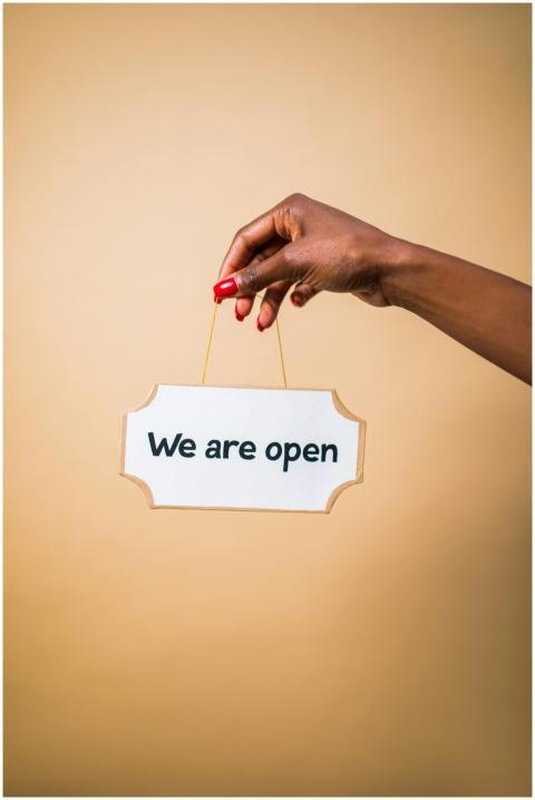 Elegant hand holding 'We are open' sign with a bei