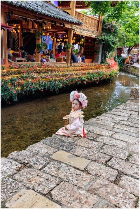 A child in traditional attire sits by a flower-lin