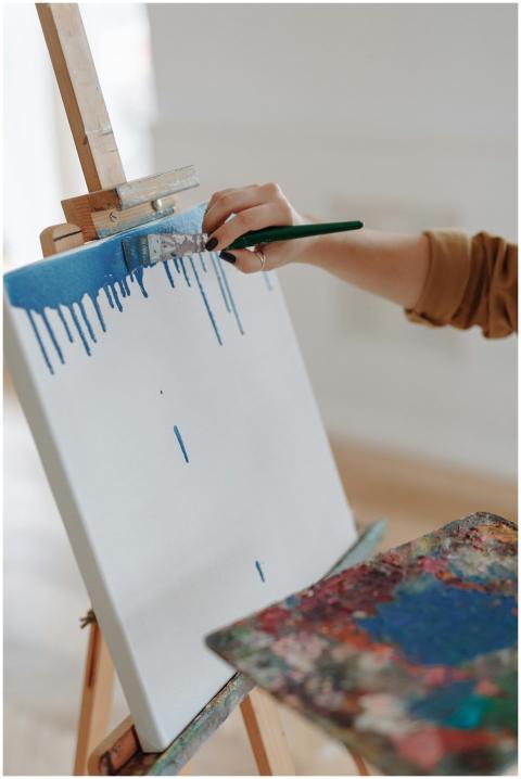 Close-up of hand painting with blue on a canvas us