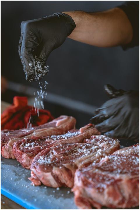 A chef seasons raw steaks with sea salt, perfectin