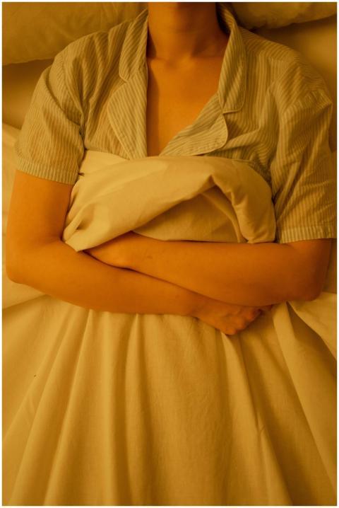 A woman in pajamas lying down in bed hugging blank