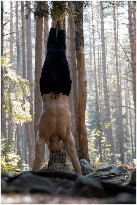 A man executes a handstand among tall trees in a s