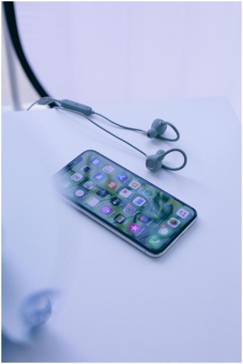 A smartphone with earphones on a white desk, showc