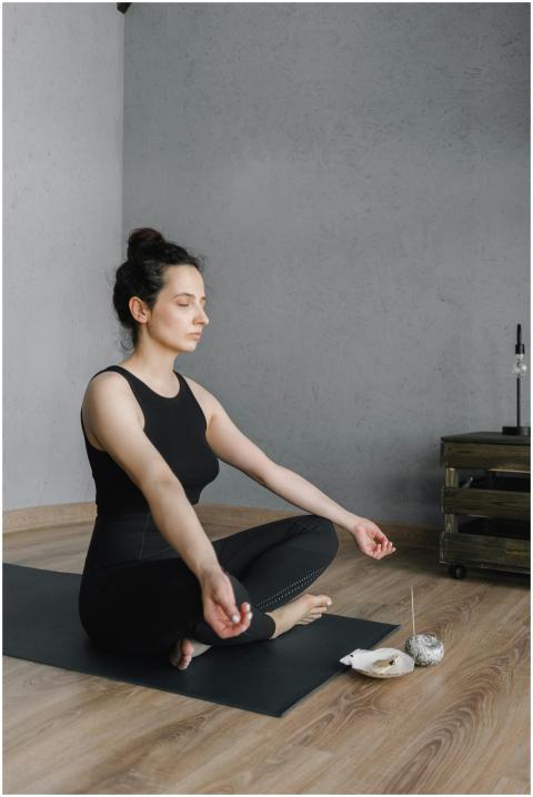 A woman in a serene pose meditates indoors, surrou