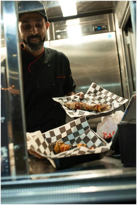A chef serves kabobs from a food truck, showcasing