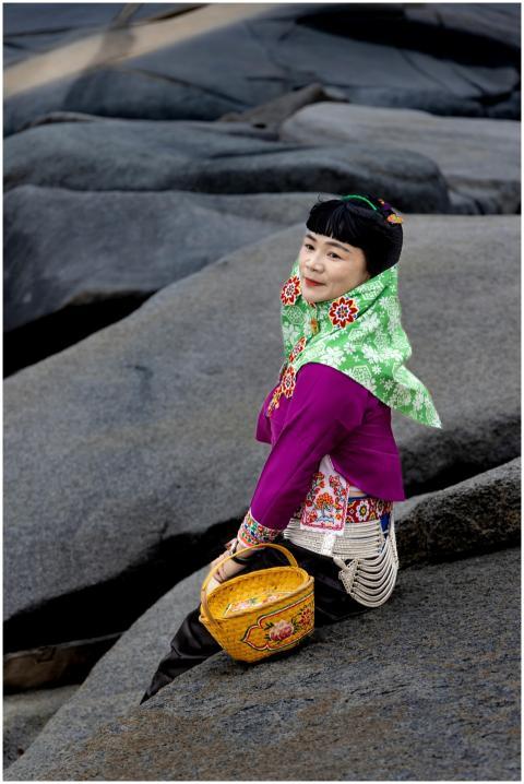 A woman in traditional clothing sits on rocks at a