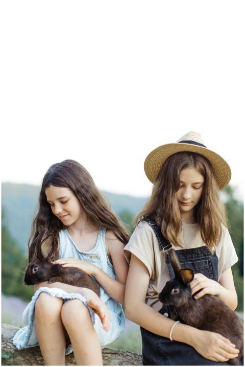 Two young girls sitting outdoors petting black rab
