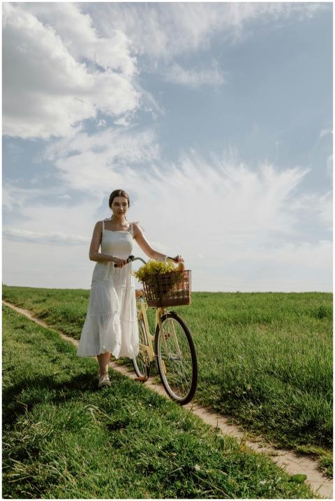 Adult woman in a white dress walking with a bicycl