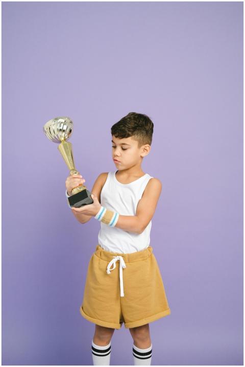 Confident young boy holding a trophy against a pas