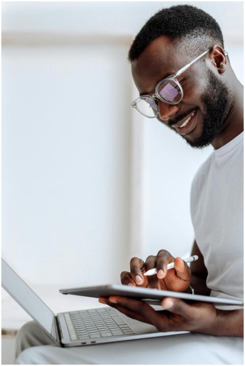 A smiling man using a tablet and laptop in a brigh