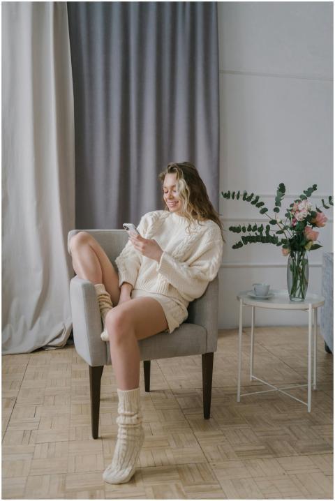 A woman in cozy attire smiles while texting on her