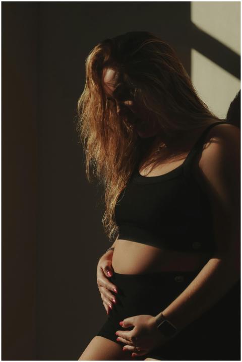 Pregnant woman standing in shadow with thoughtful