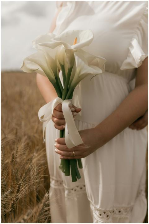 A woman in white dress holding calla lilies in a g