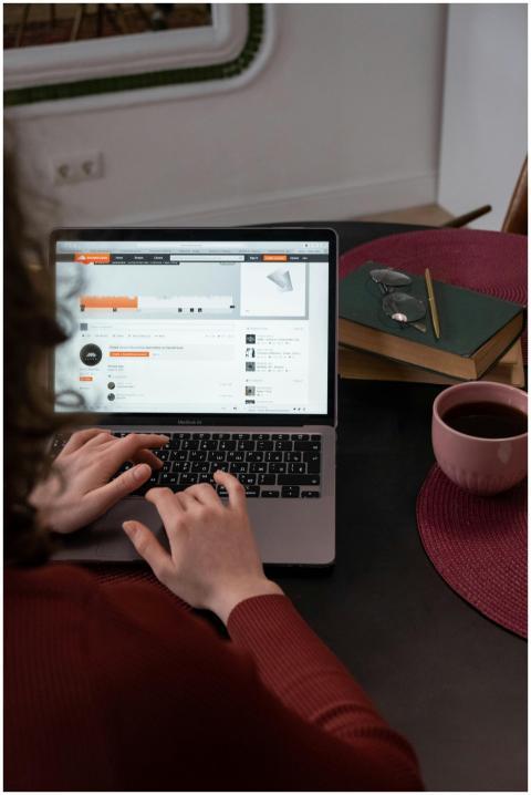 A person works on a laptop indoors, with coffee an