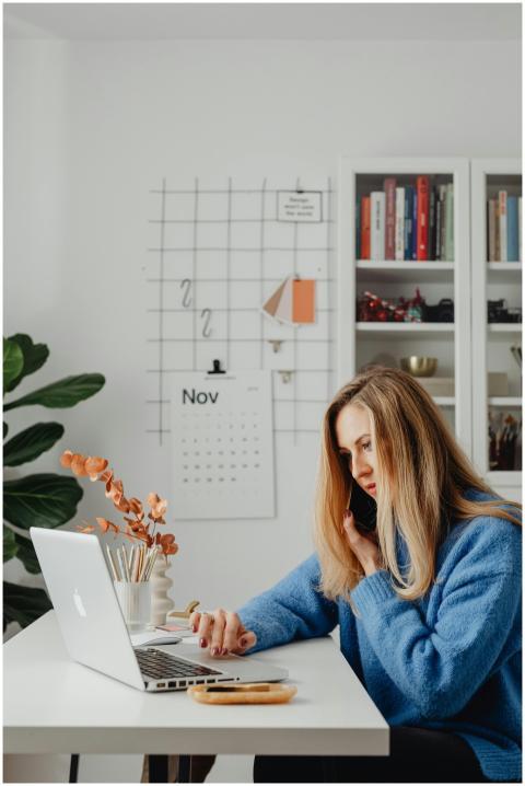 Woman multitasking at home office desk, using lapt