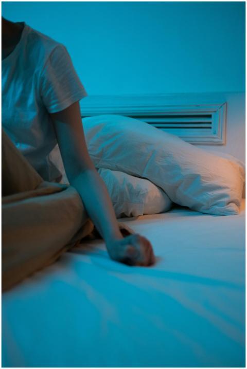 A person sitting on a bed in a dimly lit room, con