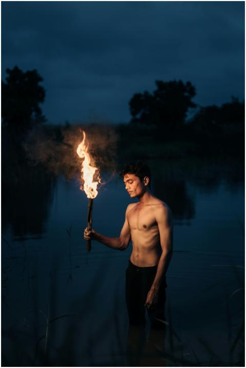 A shirtless man holds a burning torch while standi